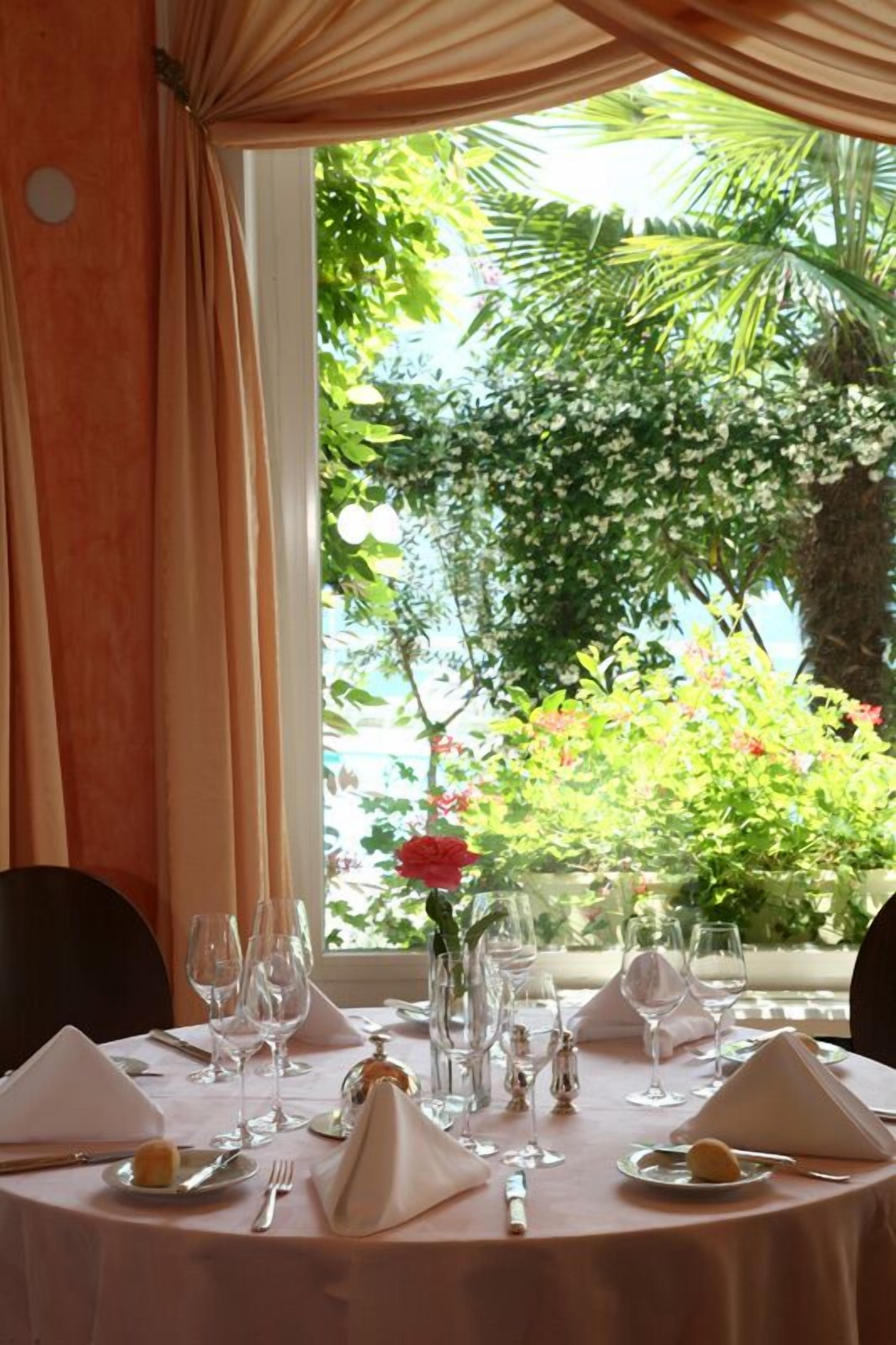 A dining table set for two with wine glasses, a vase with a single red flower, and a small dish of food.