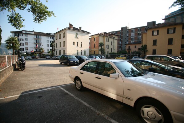 A parking lot with several cars and a motorcycle. There are multi-story buildings in the background. - Hotel Lido Seegarten (Lugano)