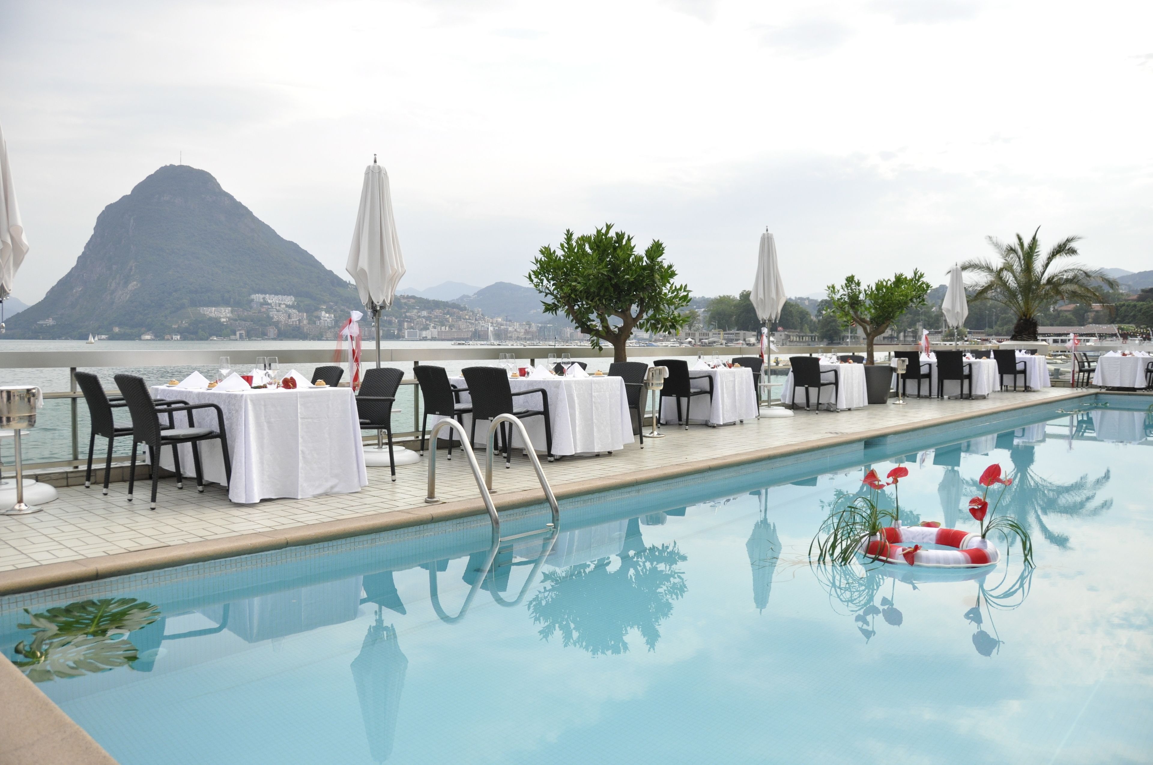 Zona de comedor junto a la piscina con mesas y sillas, un flotador salvavidas y vistas a la montaña.