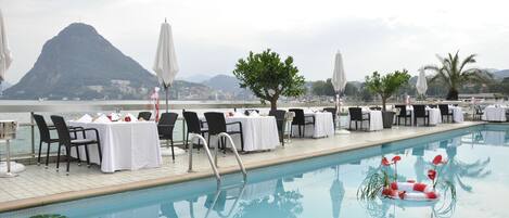 Zona de comedor junto a la piscina con mesas y sillas, un flotador salvavidas y vistas a la montaña.