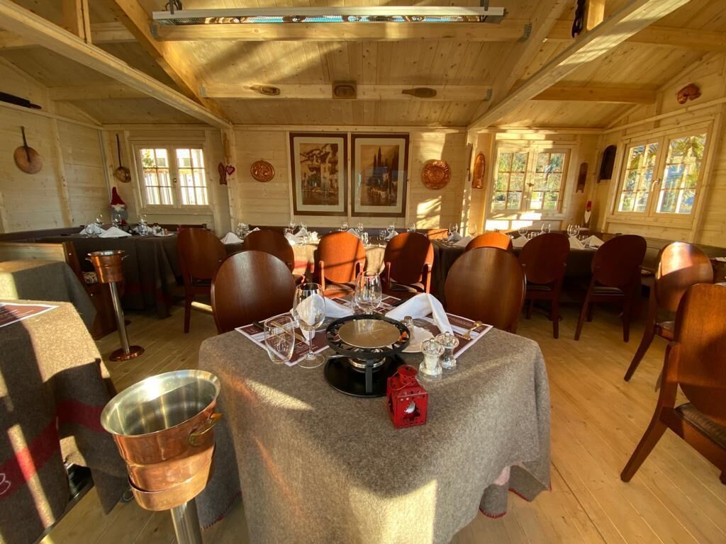 A dining area with wooden tables and chairs, framed artwork on the walls, and large windows allowing natural light.