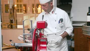 Un chef con uniforme y gorro blanco parado en una cocina con un cortador de carne rojo, marcado con