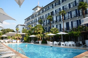Zona de piscina de hotel con múltiples sillas de descanso, sombrillas y una piscina azul cristalina.