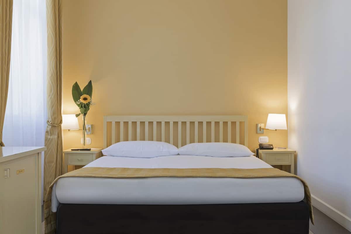 A neatly made bed with white linens, a wooden headboard, and two bedside lamps.