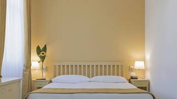 Uma cama bem arrumada com lençóis brancos, cabeceira de madeira e duas luminárias laterais.