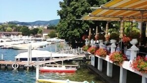Un puerto deportivo con barcos amarrados, un flotador salvavidas y un edificio con una zona cubierta y macetas con flores.