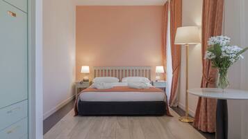 A hotel room with a bed, nightstands, a lamp, a vase with flowers, and a wardrobe.