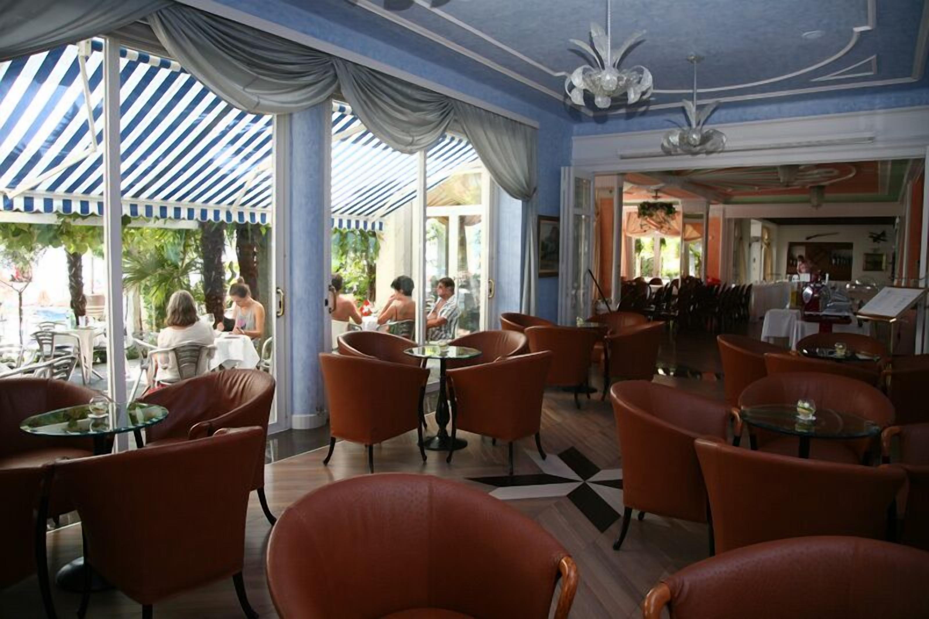 Una hall d'albergo con poltrone in pelle arancione, pavimento a motivi e un tendone a righe blu e bianche.