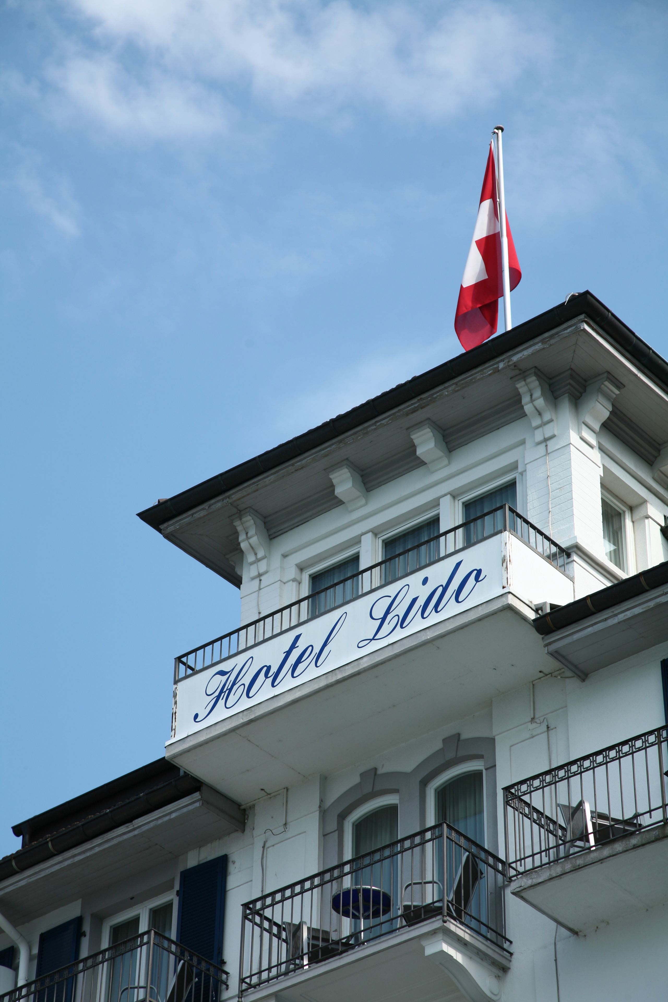 Ett hotell som heter ”Hotel Lido”, med en flagga på taket, balkonger och en klar himmel i bakgrunden.