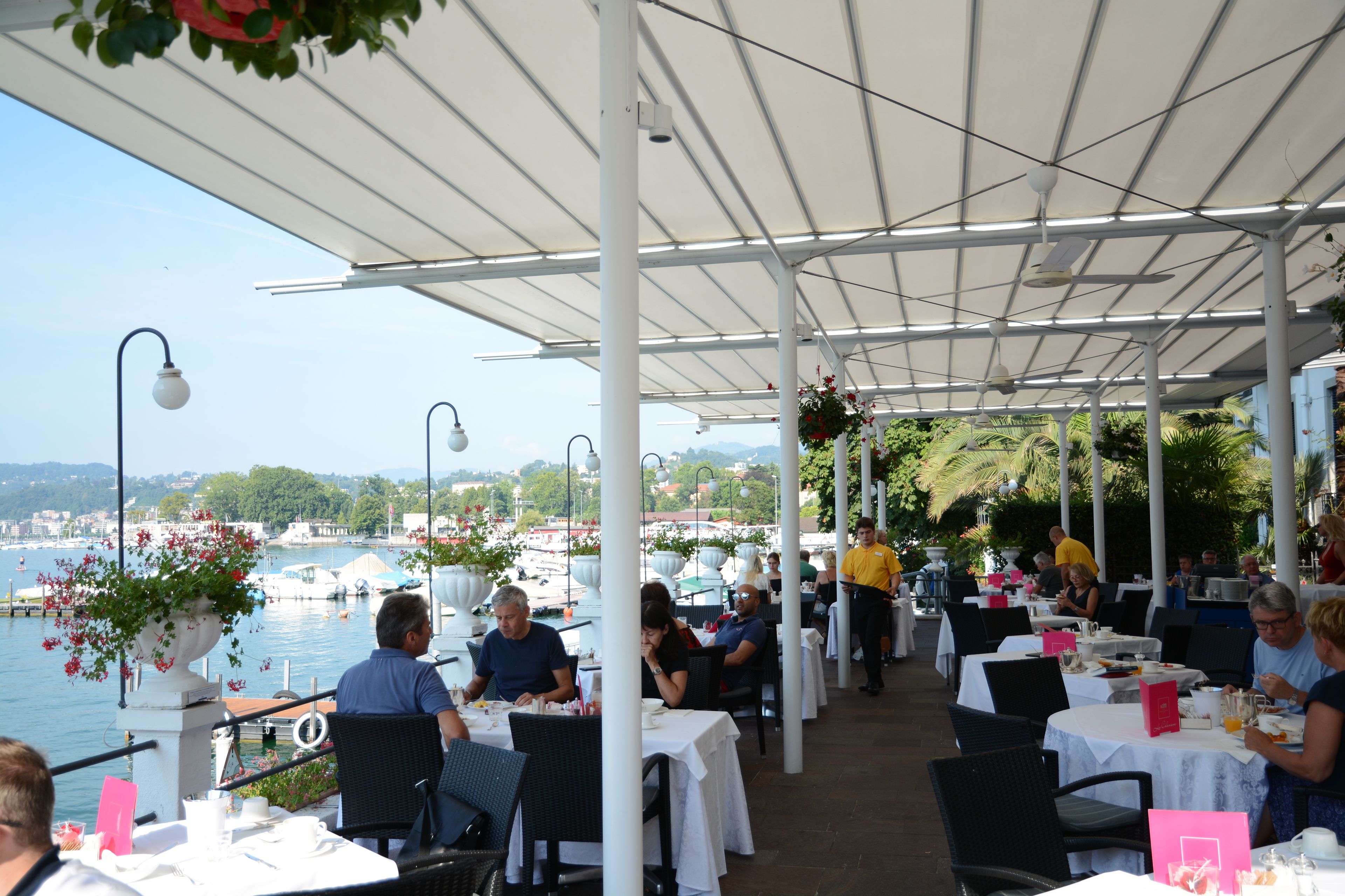 An outdoor dining area with tables and chairs, overlooking a body of water and a distant town.