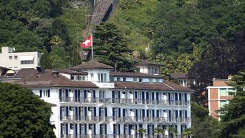 A multi-story hotel with balconies, surrounded by lush greenery and a railway track.