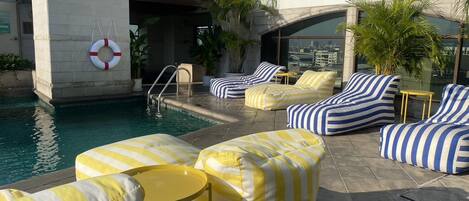 Un área de piscina en la azotea con sillas de descanso a rayas y una pequeña mesa.