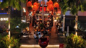 An indoor dining area with tables and chairs, surrounded by palm trees and decorative lights.