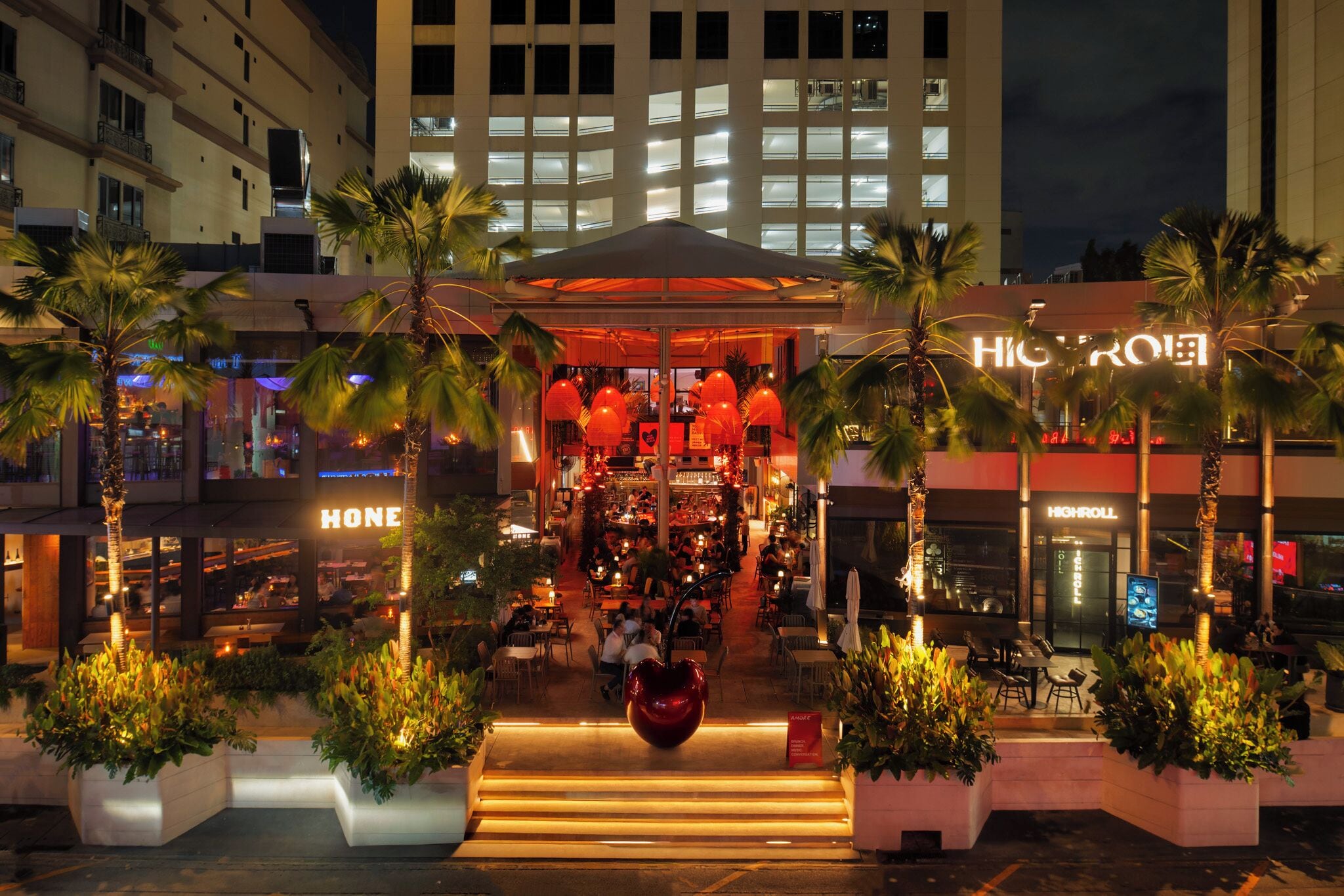 A hotel entrance with a covered outdoor seating area, palm trees, and a heart-shaped sculpture.