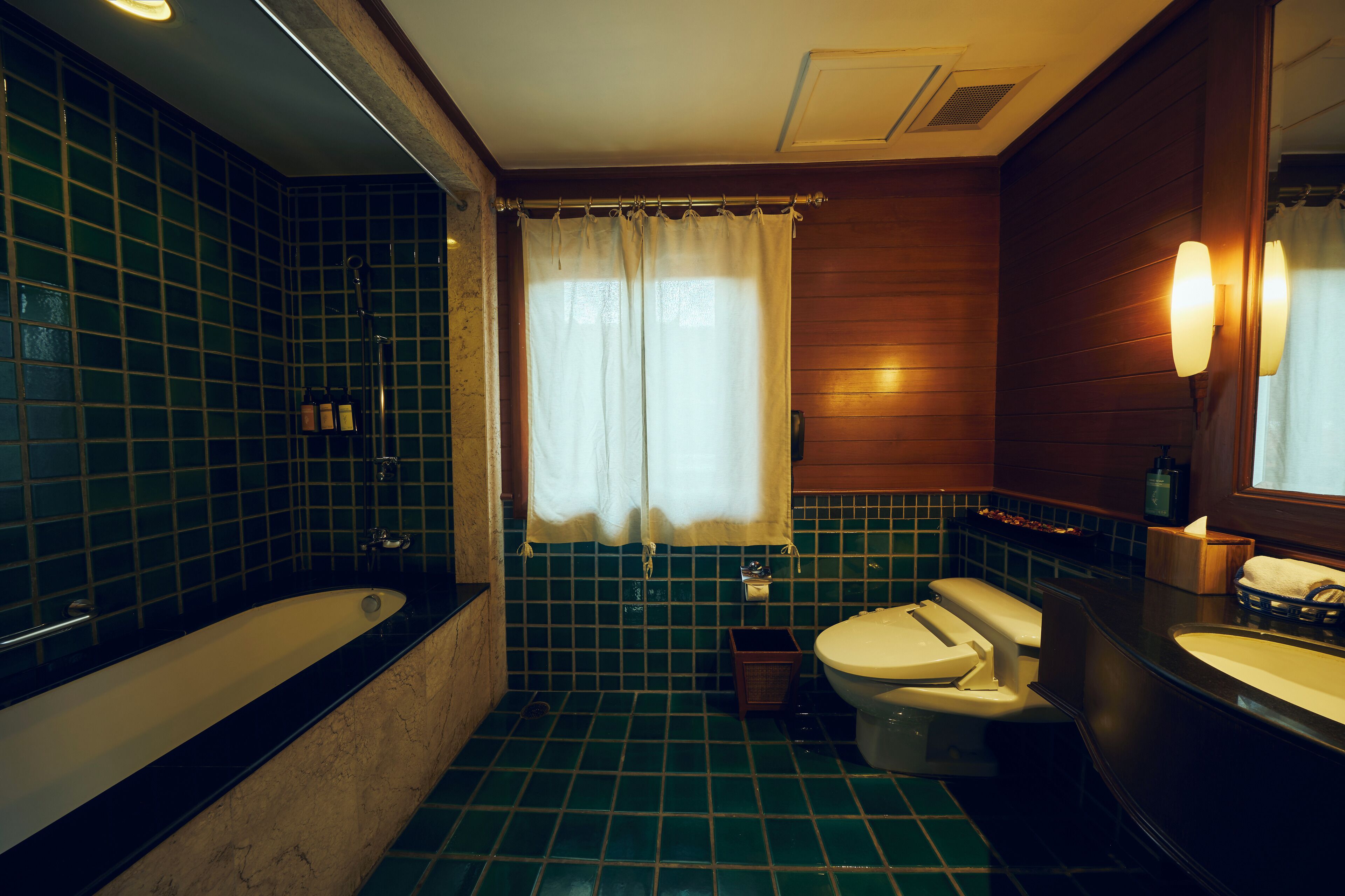 A bathroom with a bathtub, toilet, and sink, featuring green tiles and wooden paneling.