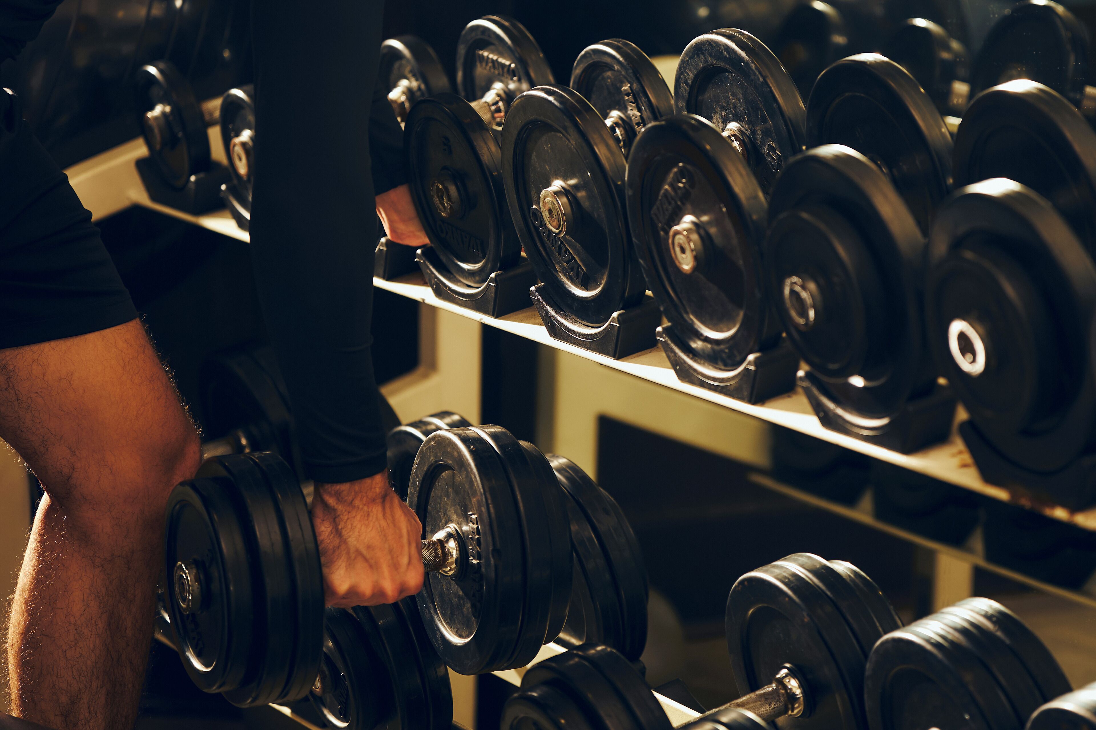 A person lifting a dumbbell from a rack of similar weights.