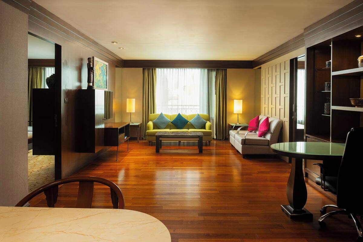 Une chambre d’hôtel avec un plancher en bois, un canapé agrémenté de coussins colorés, une table à manger et un téléviseur.