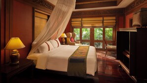 A spacious bedroom with a large bed, a nightstand with a lamp, a chair, and a wardrobe.