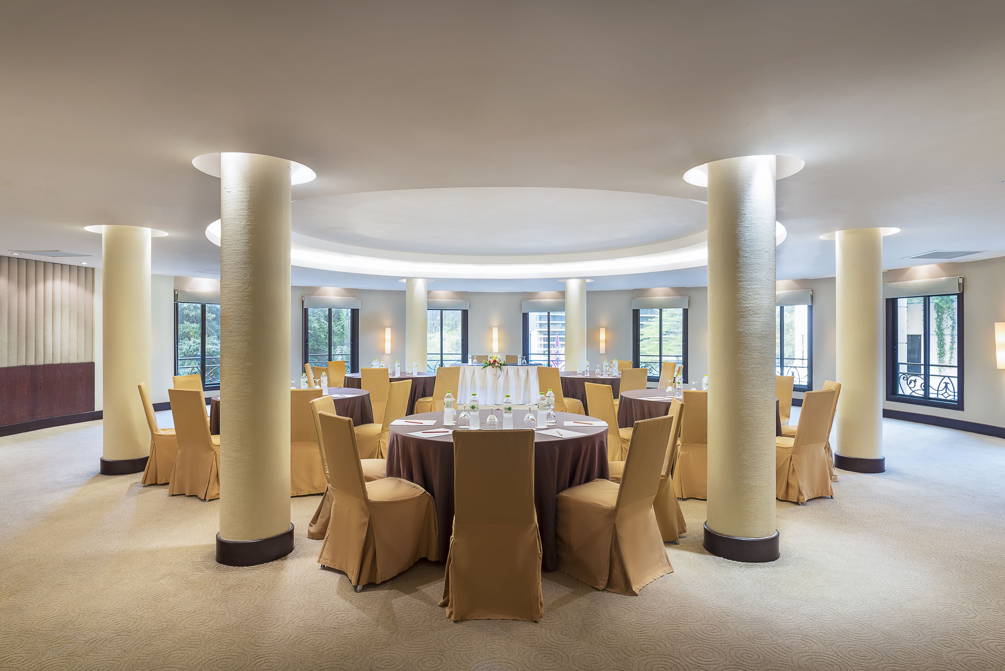 A large, circular room with round tables and chairs, large columns, and large windows.