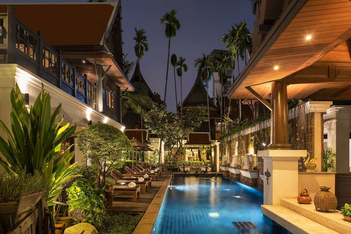 Un espace aménagé au bord de la piscine, avec des chaises longues, une piscine et des plantes tropicales.
