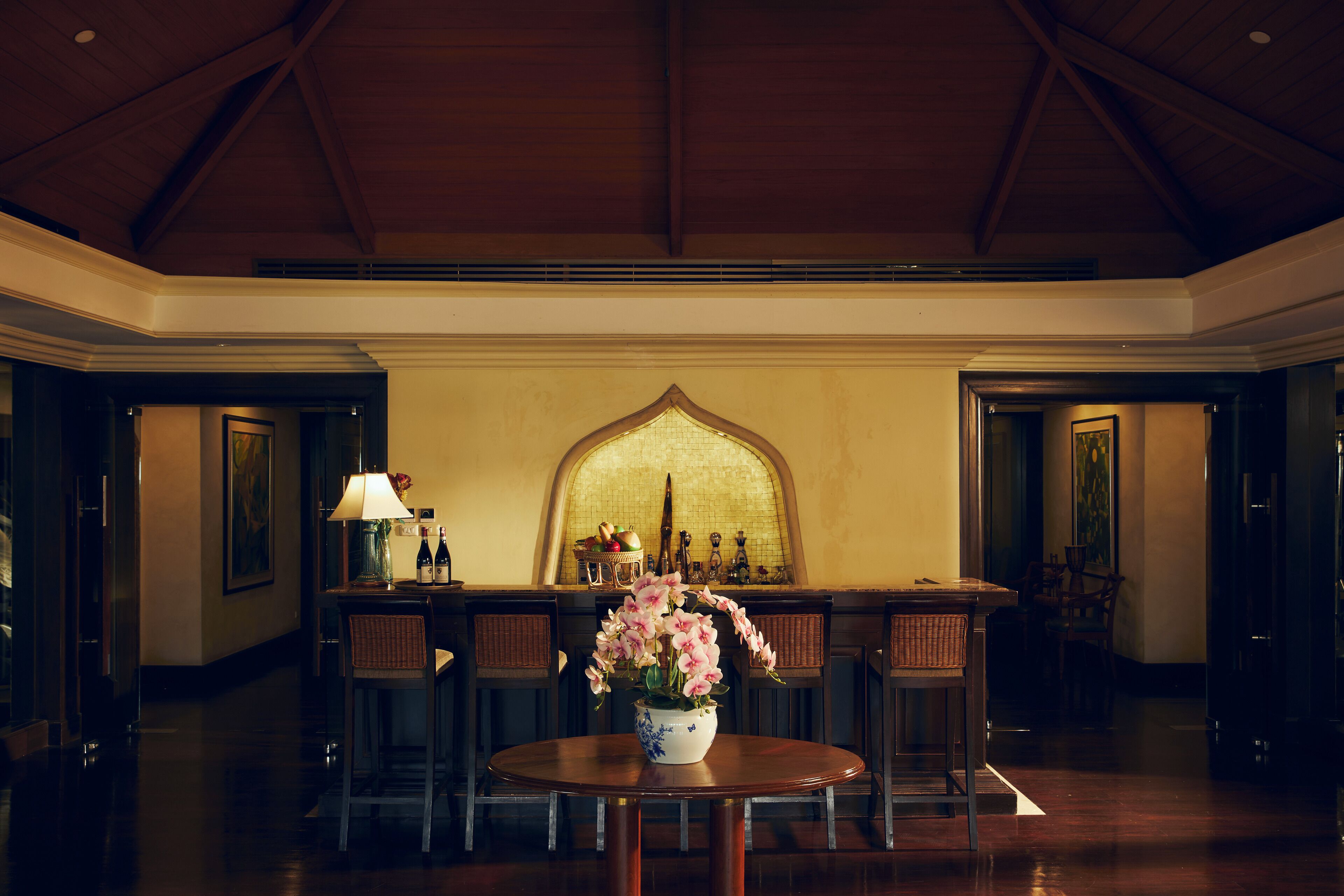 A bar area with a round table, chairs, and a vase of flowers.