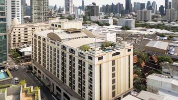 A high-rise hotel with multiple floors, a rooftop pool, and a city skyline in the background.