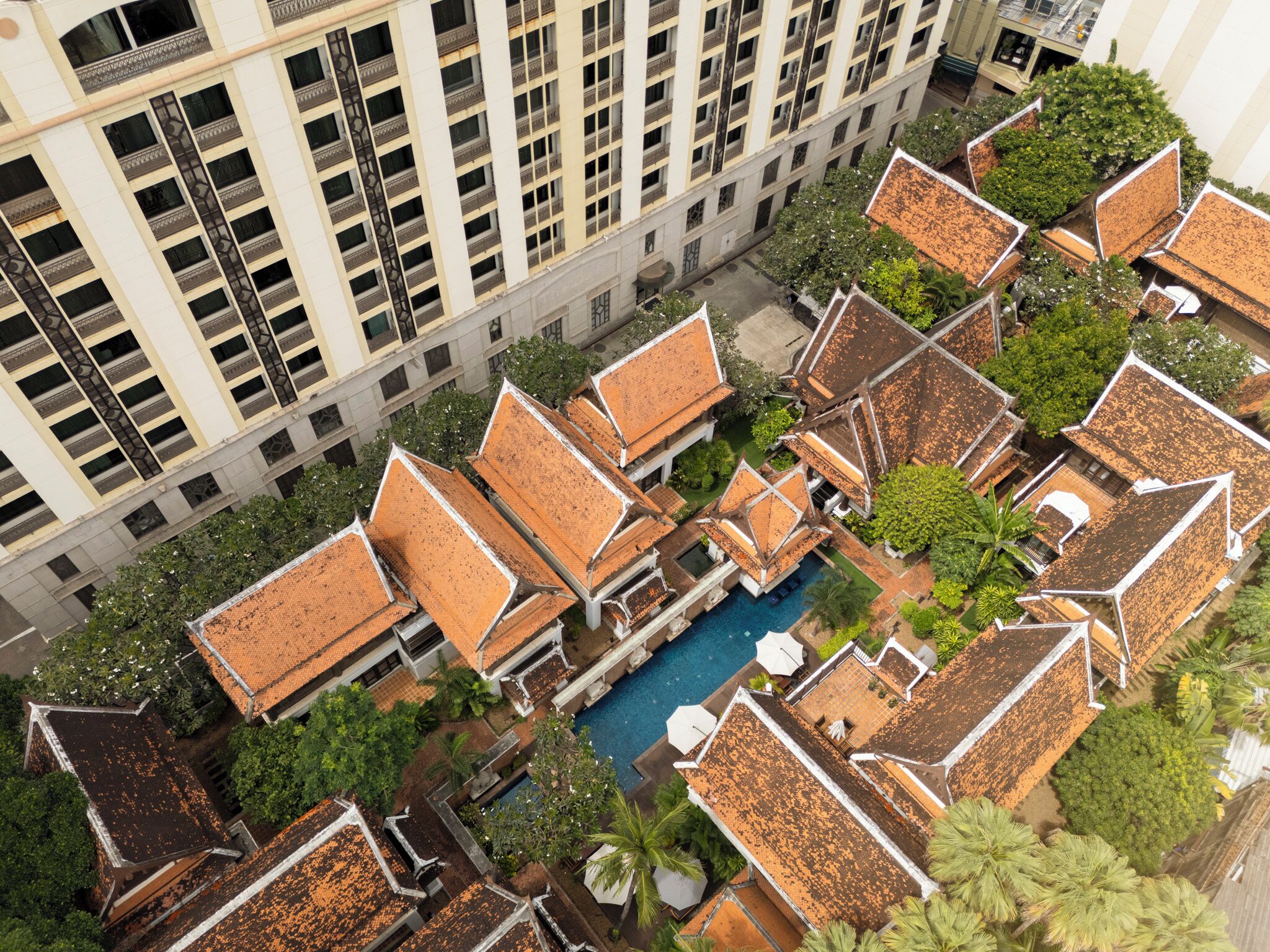 Een hoog hotel met meerdere balkons en een zwembad omringd door weelderige begroeiing.