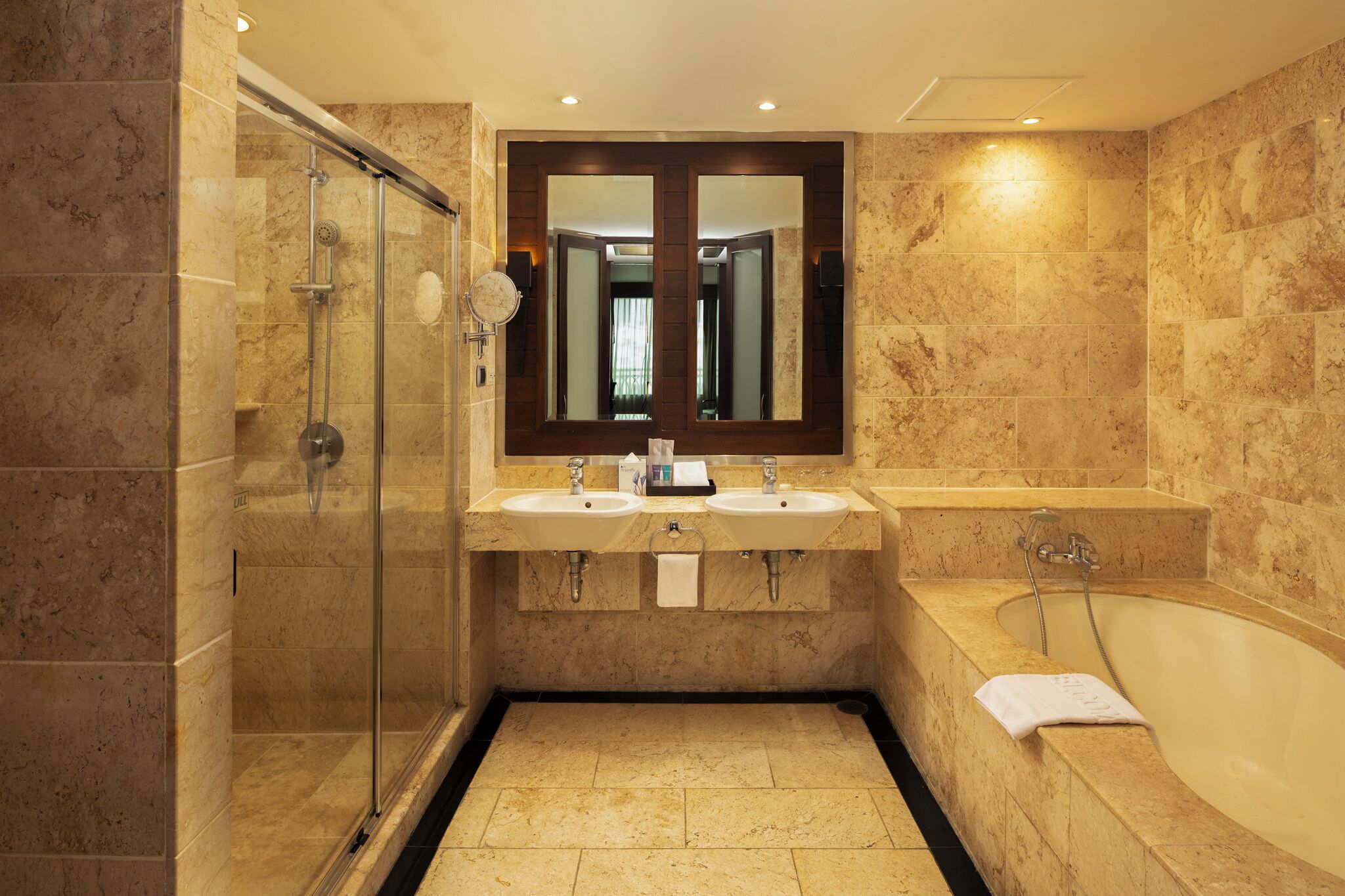 A bathroom with a glass-enclosed shower, two sinks, a large mirror, and a bathtub.