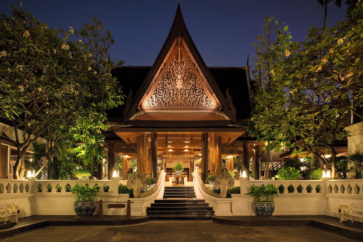 Un bâtiment traditionnel thaïlandais, orné de sculptures complexes, avec un escalier menant à l’entrée et des plantes en pot disposées le long du chemin.