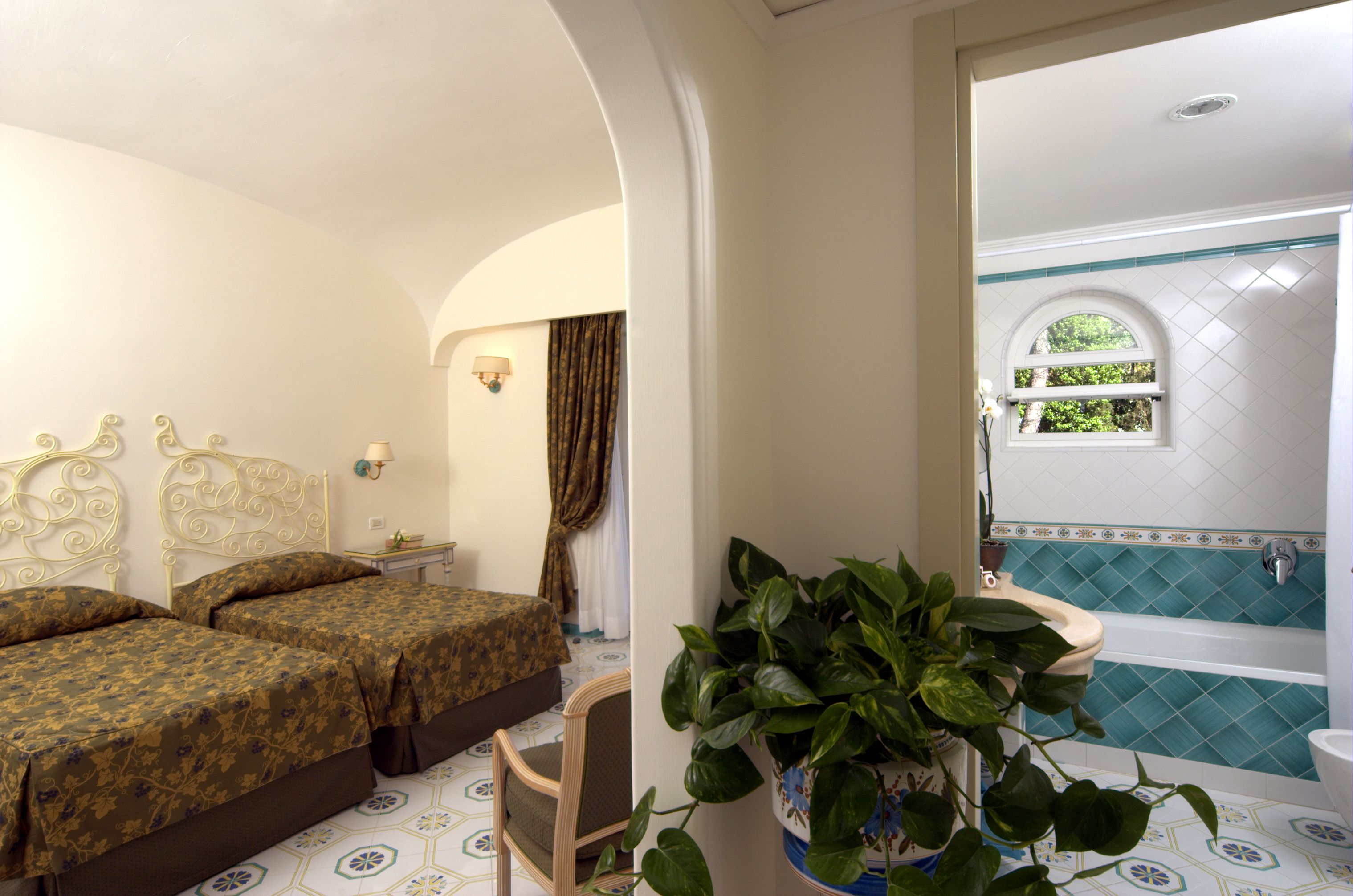 Ein Zimmer mit zwei Betten, einem Blumentopf, einem Badezimmer mit Badewanne und einem Fenster mit Blick auf Grünflächen.