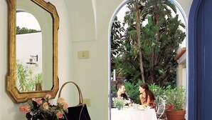 A hallway with a mirror, a vase with flowers, and a table set for two outside. - Grand Hotel Il Moresco & Spa (Ischia)
