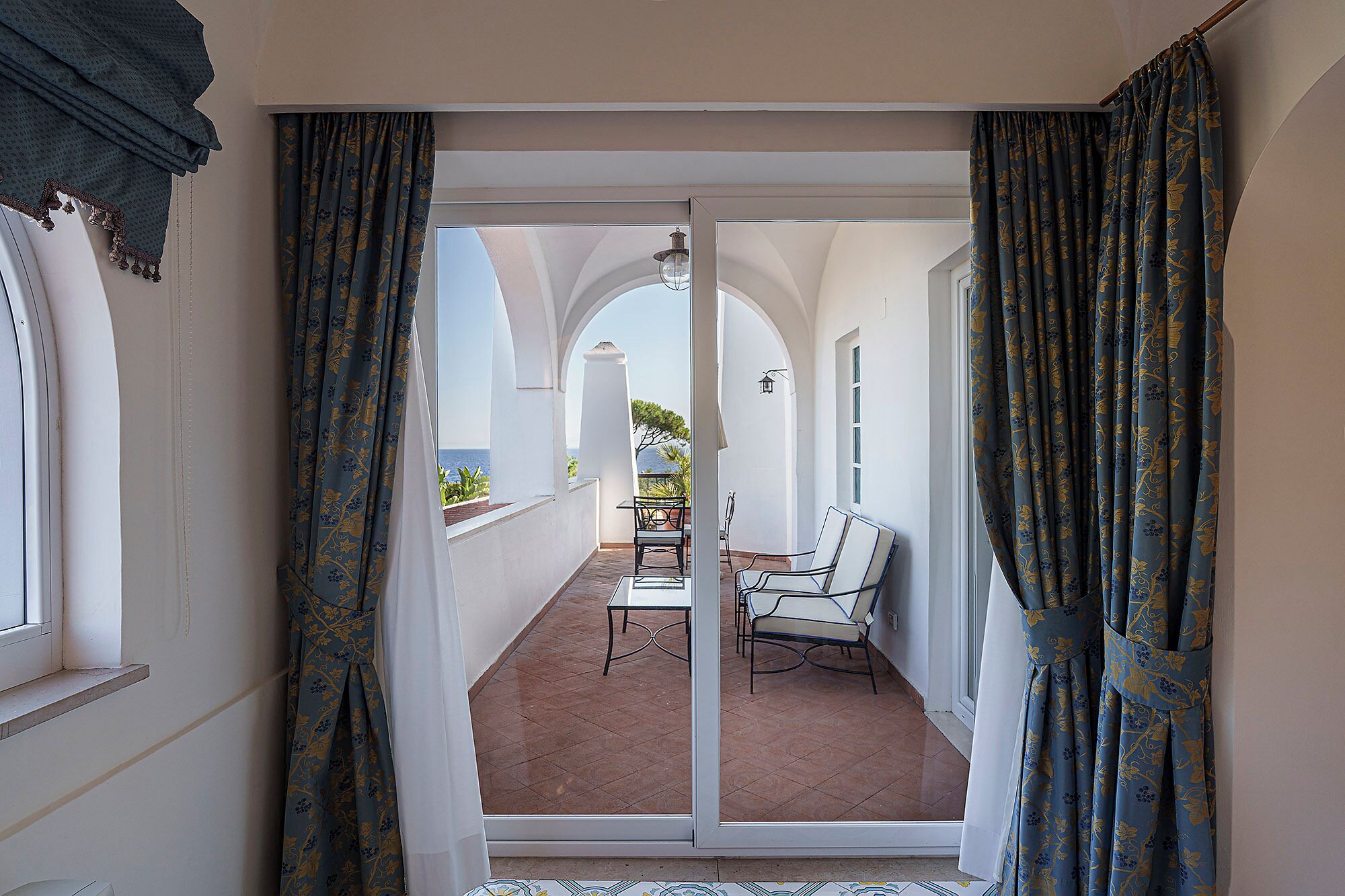 A balcony with a view of the sea, white walls, and a table with chairs.