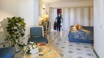 Habitación de hotel con cama, una silla, una mesa con un jarrón de flores y una planta en maceta.