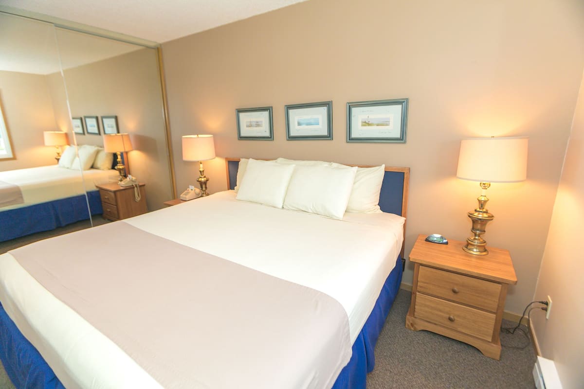 Quarto de hotel com uma cama grande, mesas de cabeceira, um espelho e quadros nas paredes.