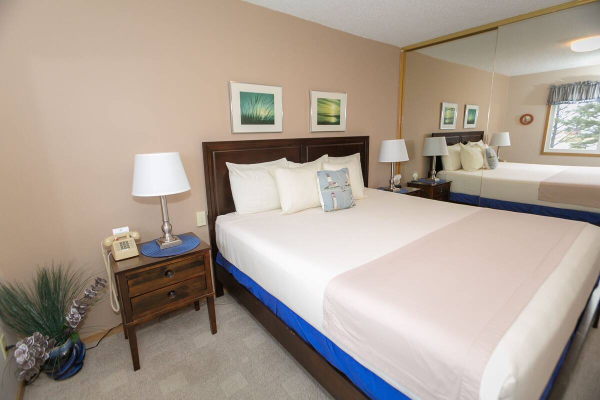 Quarto de hotel com uma cama grande, duas mesas de cabeceira, um espelho e um vaso de planta.
