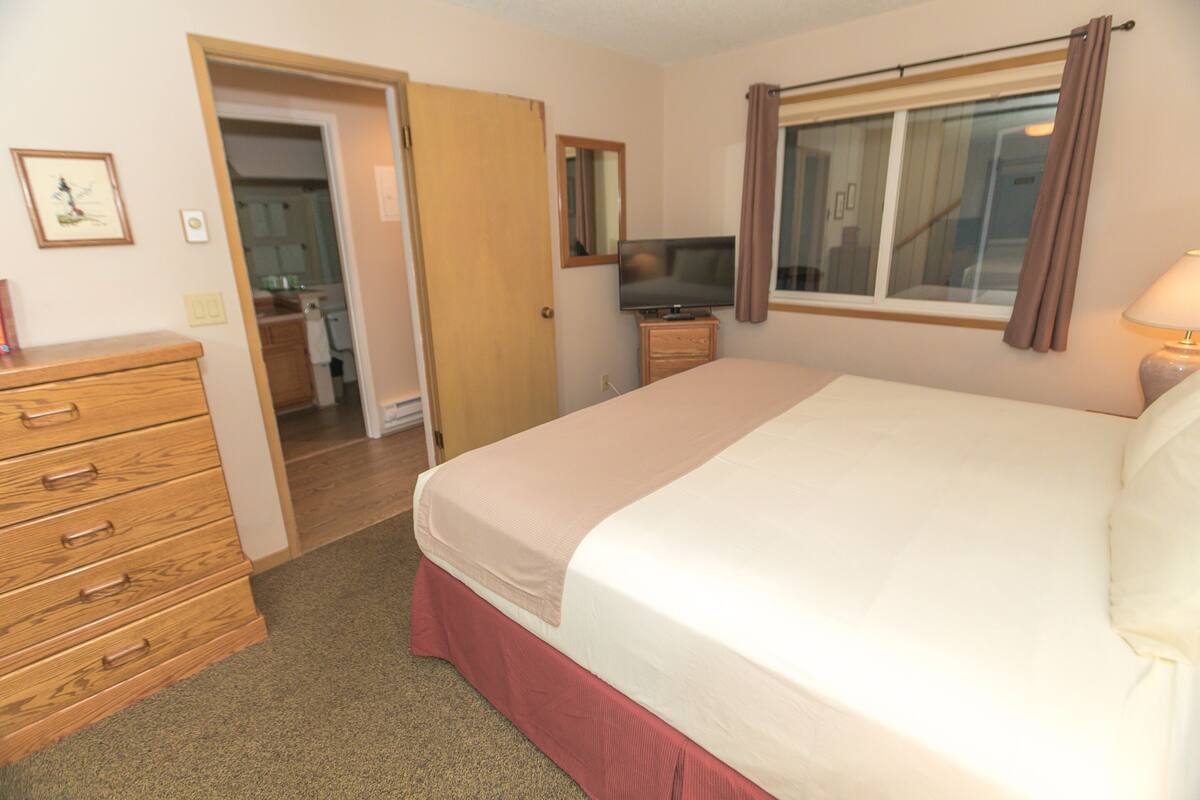 Quarto de hotel com cama, penteadeira, televisão e janela com cortinas.