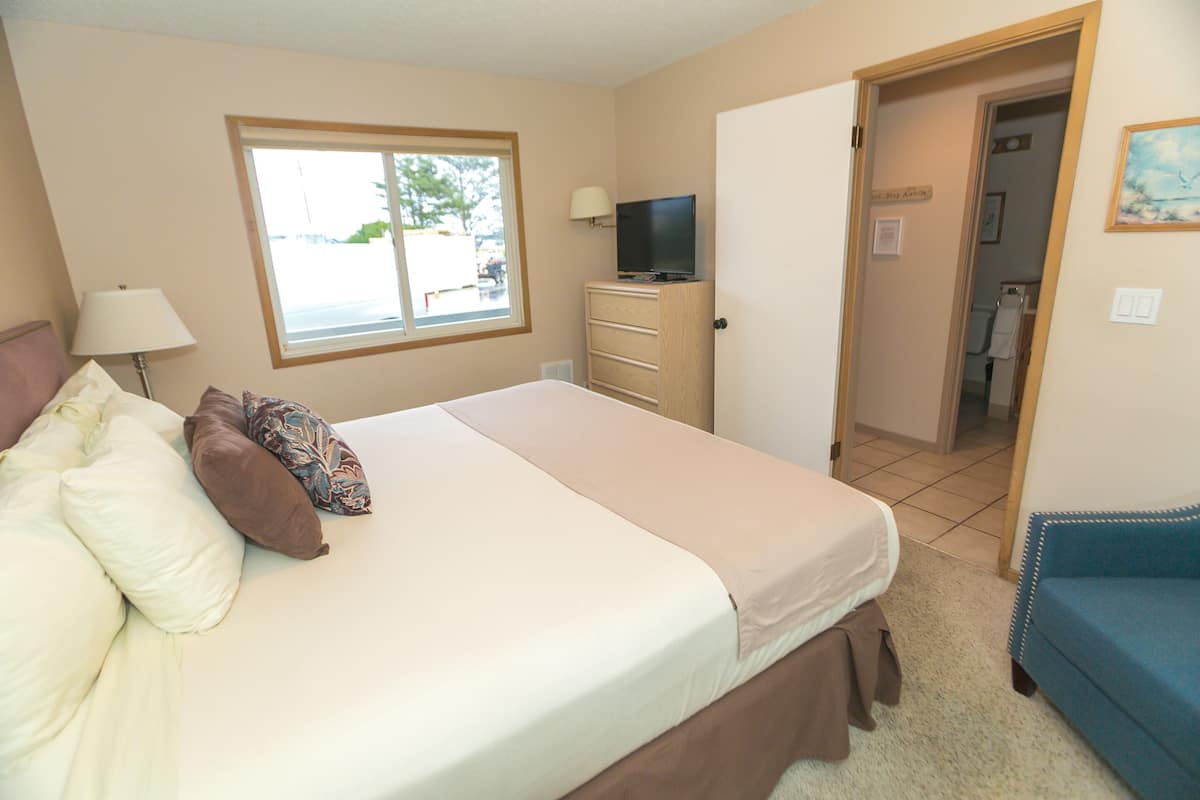 Quarto de hotel com uma cama, televisão, penteadeira, janela e porta que dá para um banheiro.