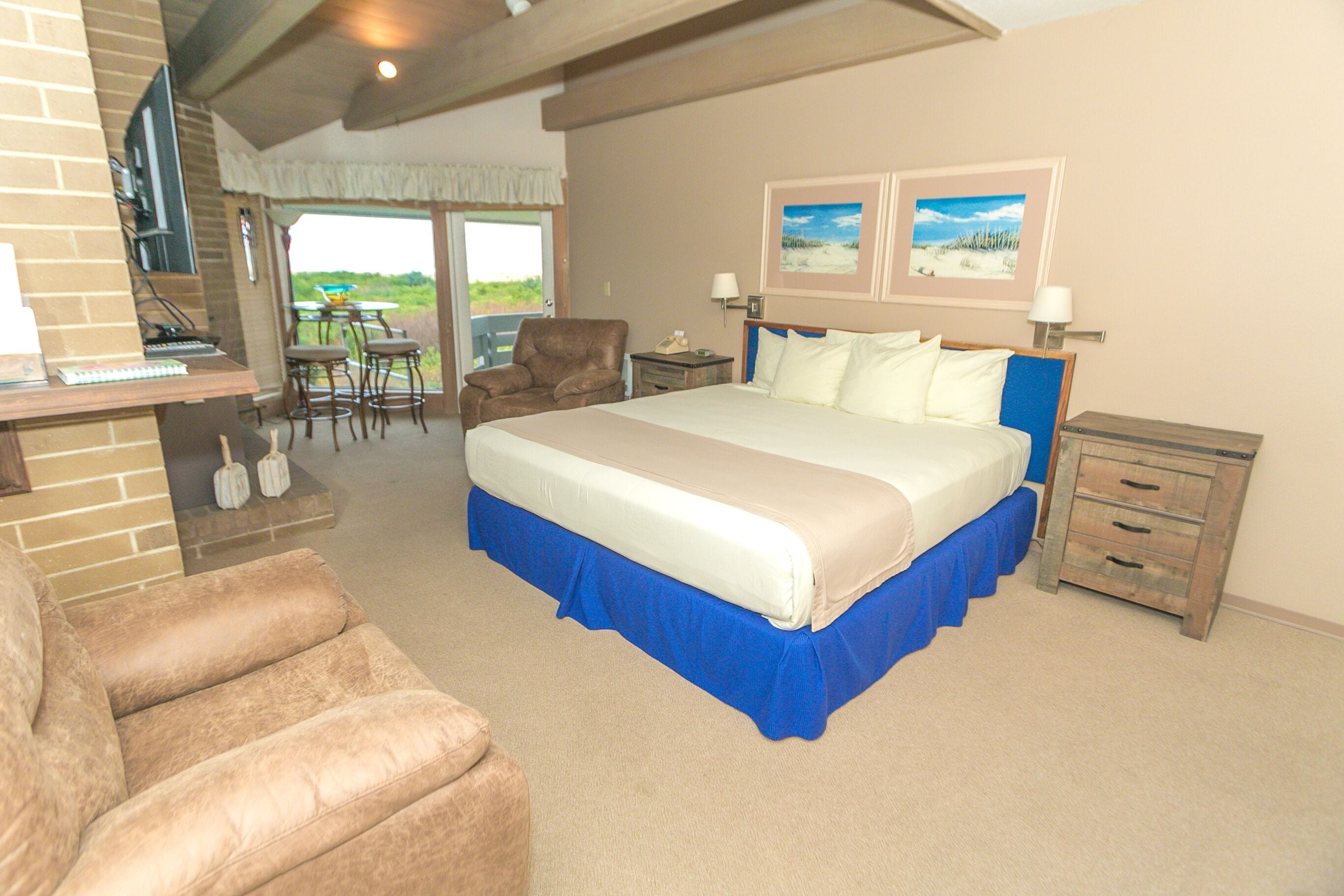 A bedroom with a large bed, a desk with a computer, a chair, and a view of the outdoors.