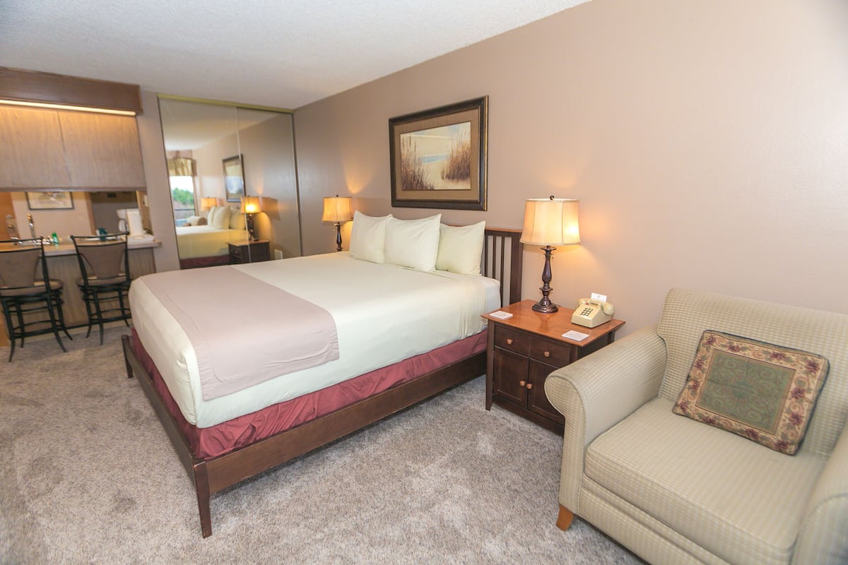 Quarto de hotel com cama, escrivaninha, cadeira, mesa de cabeceira com abajur e sofá.