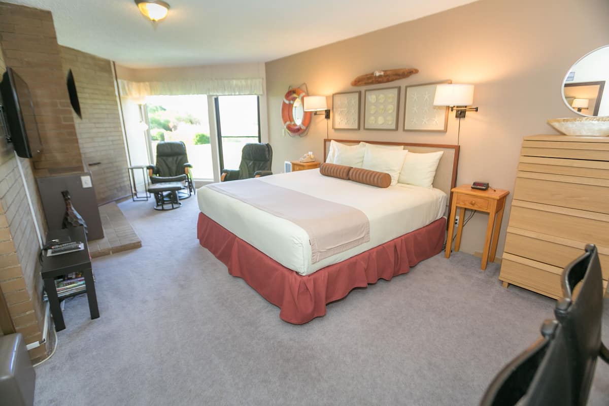 Quarto de hotel com uma cama grande, penteadeira de madeira, televisão, cadeira e escrivaninha.