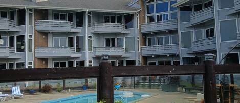 A residential building with multiple balconies, a swimming pool, and a fenced patio area with lounge chairs.