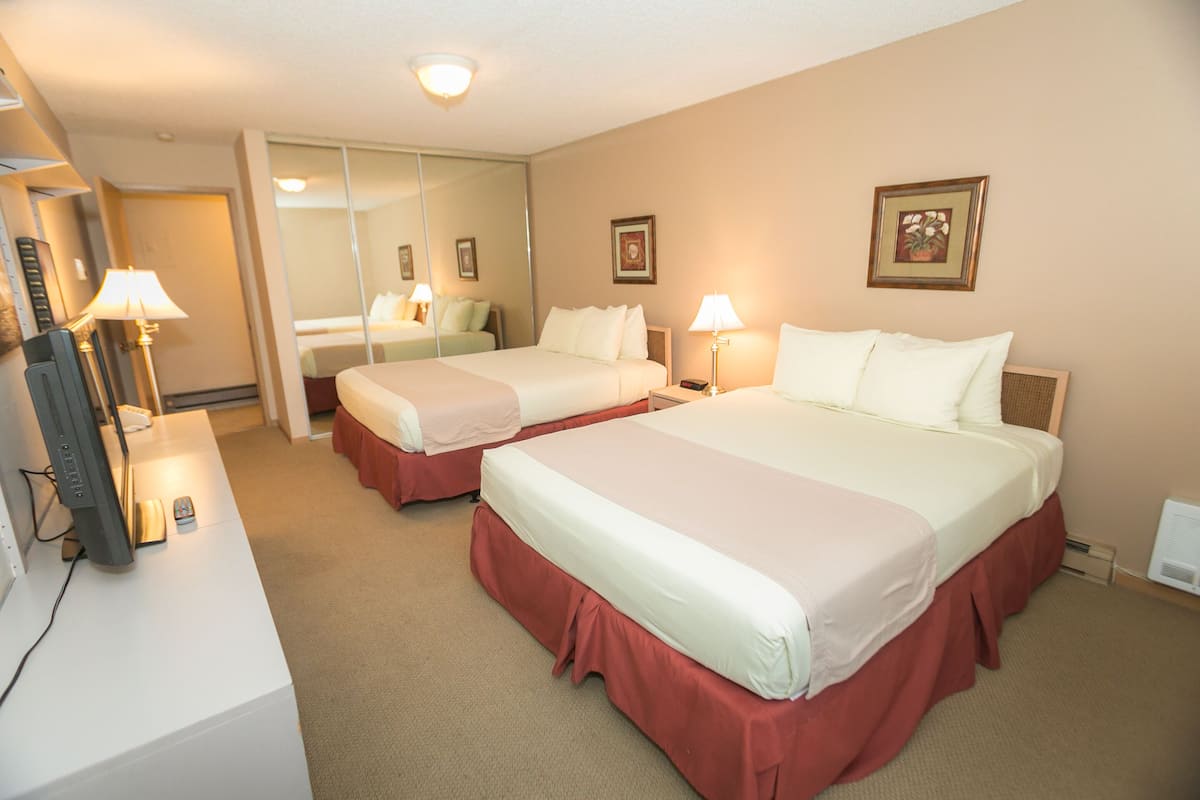 Quarto de hotel com duas camas, uma escrivaninha com computador e um espelho.