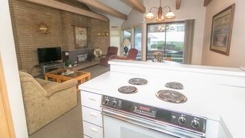 A kitchen with a white stove, a dining table, and a sofa in a living room area.