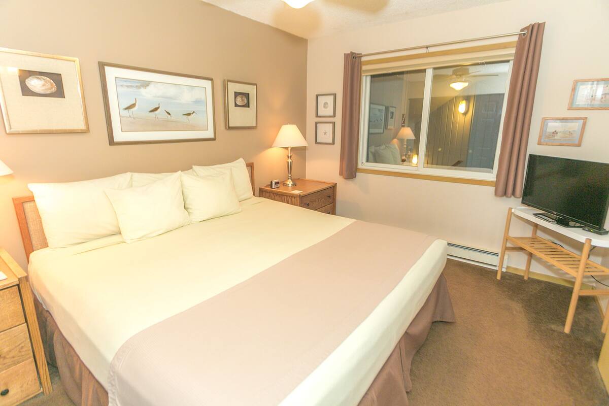 Quarto de hotel com uma cama grande, uma escrivaninha com computador e quadros nas paredes.
