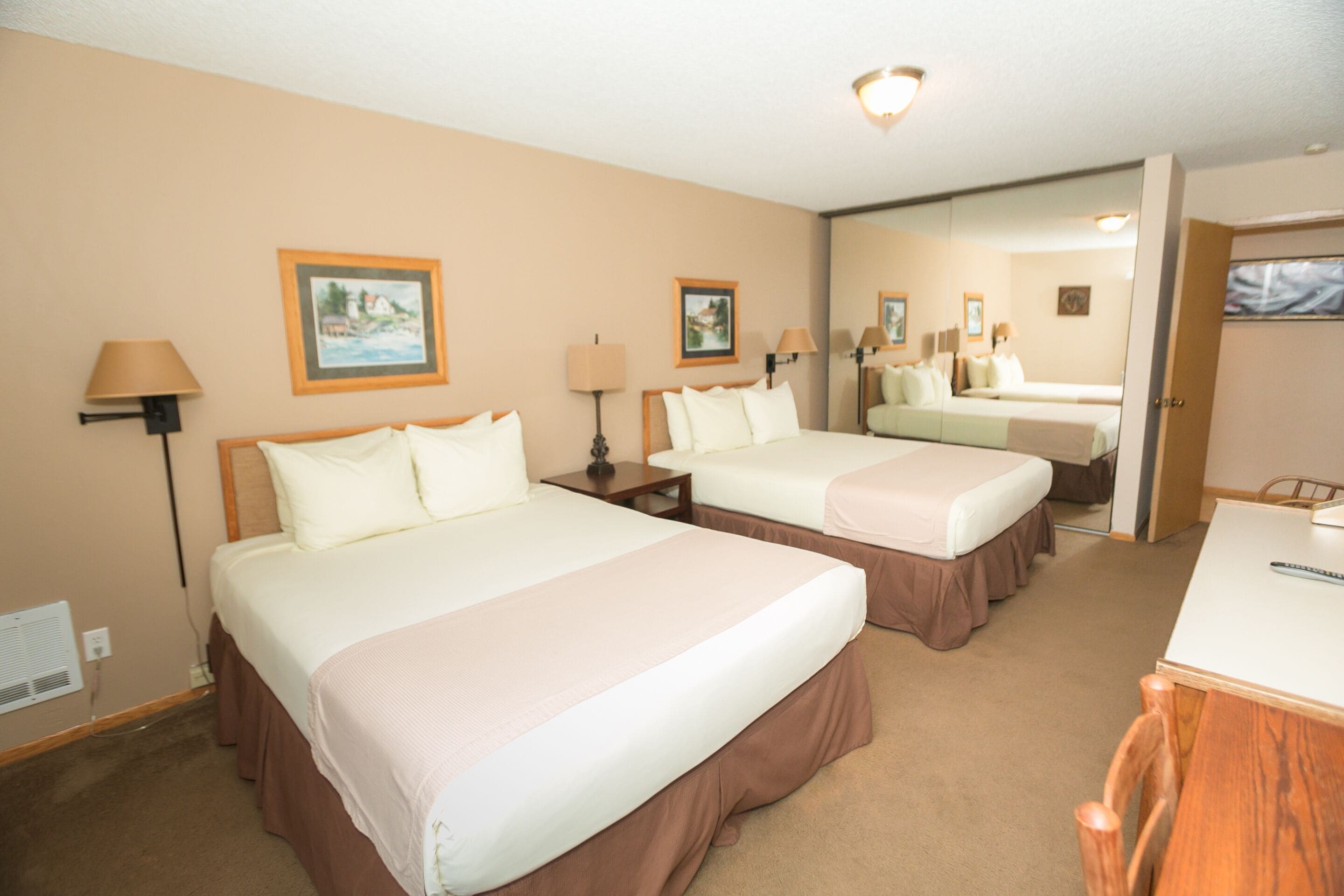 A hotel room with two beds, a desk, and a mirror.