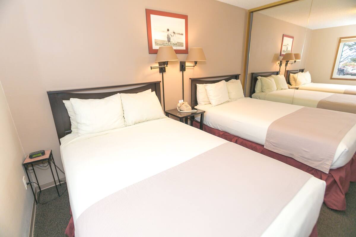 Quarto de hotel com duas camas, uma mesa de cabeceira com telefone e um espelho na parede.