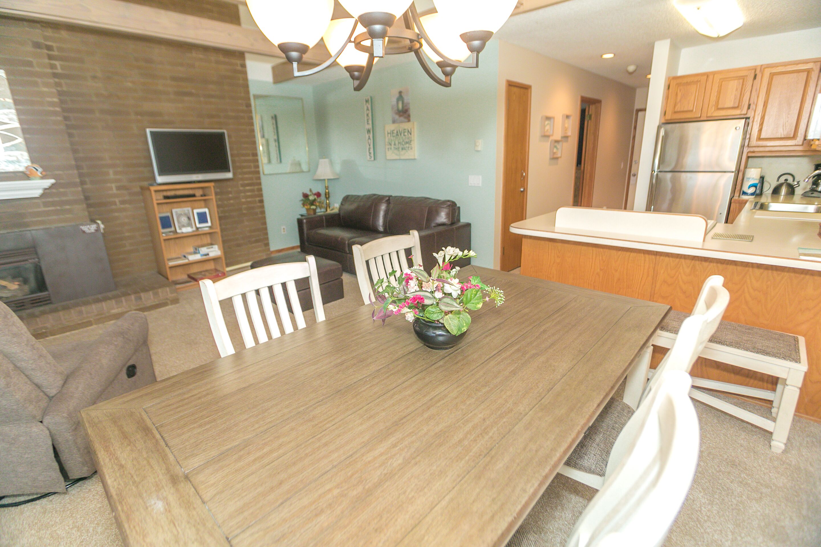 A dining area with a wooden table, white chairs, and a vase of flowers.