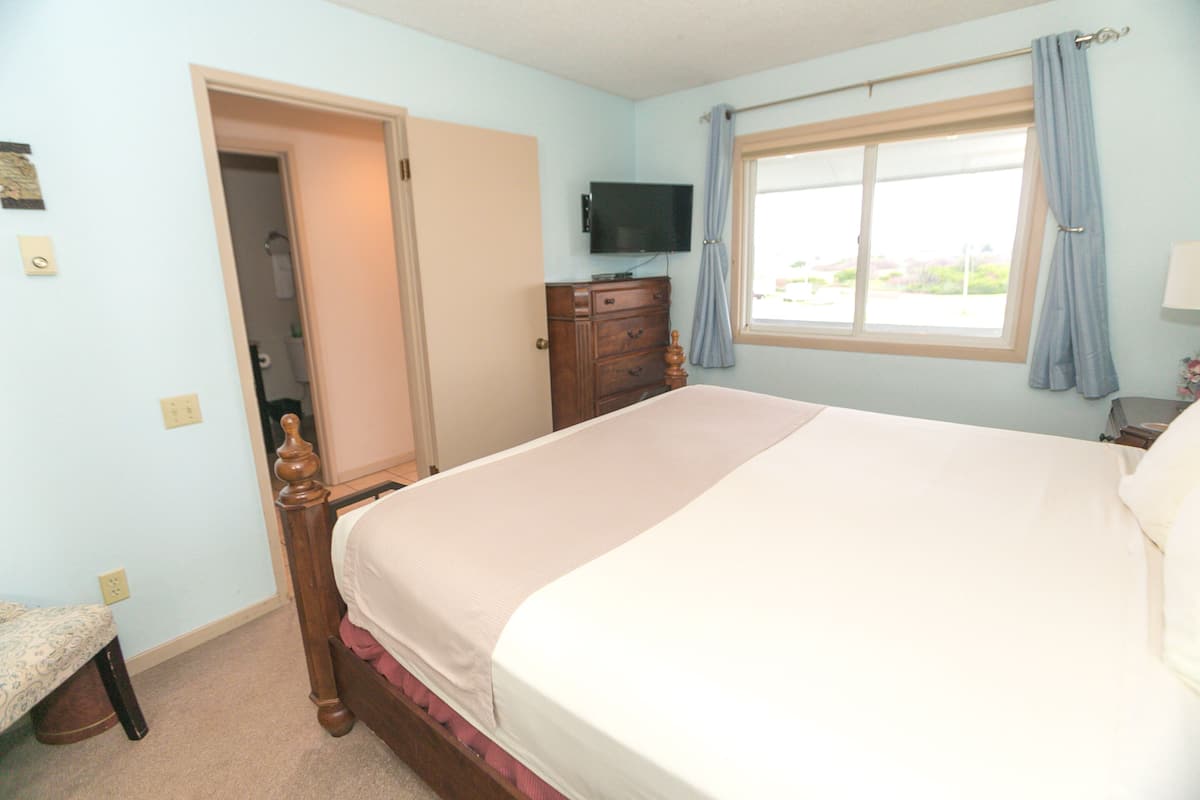 Quarto com cama, cômoda, televisão e janela com cortinas.