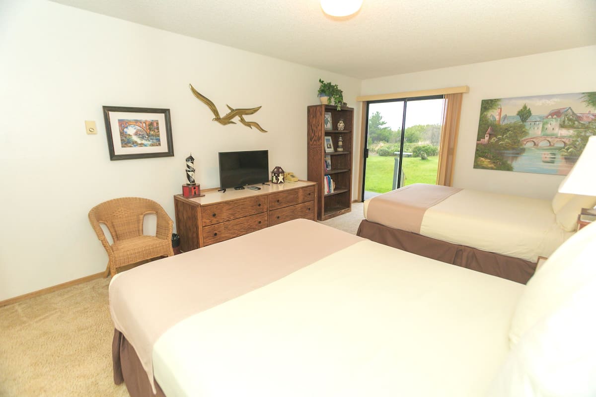Quarto de hotel com duas camas, televisão, estante e vista para o exterior.