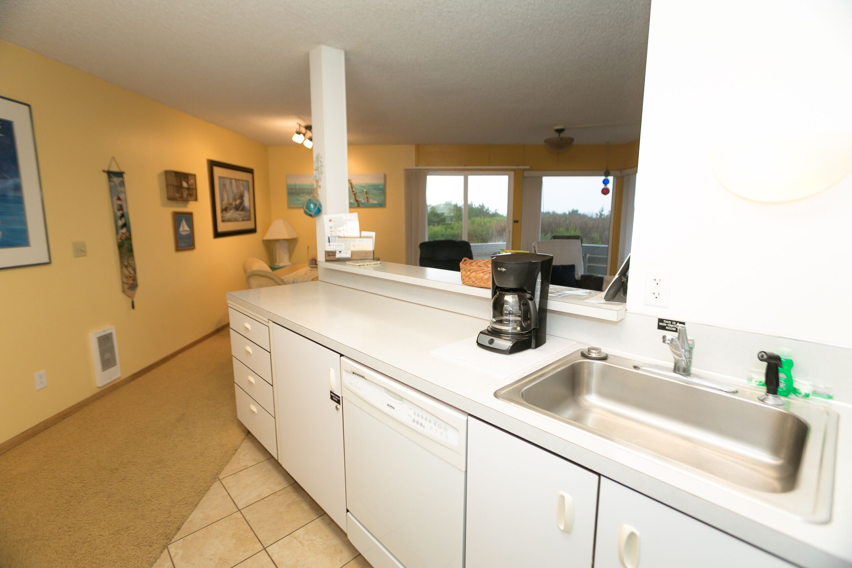 A kitchen with white cabinets, a dishwasher, a coffee maker, and a sink.